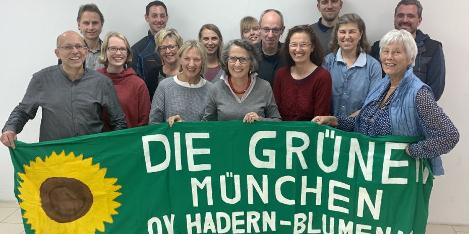 Gruppe von OV-Mitgliedern, die ein Grüns Tuch mit dem Text Die Grünen München OV Hadern-Blumenau sowie einer gemalten Sonnenblume halten.
